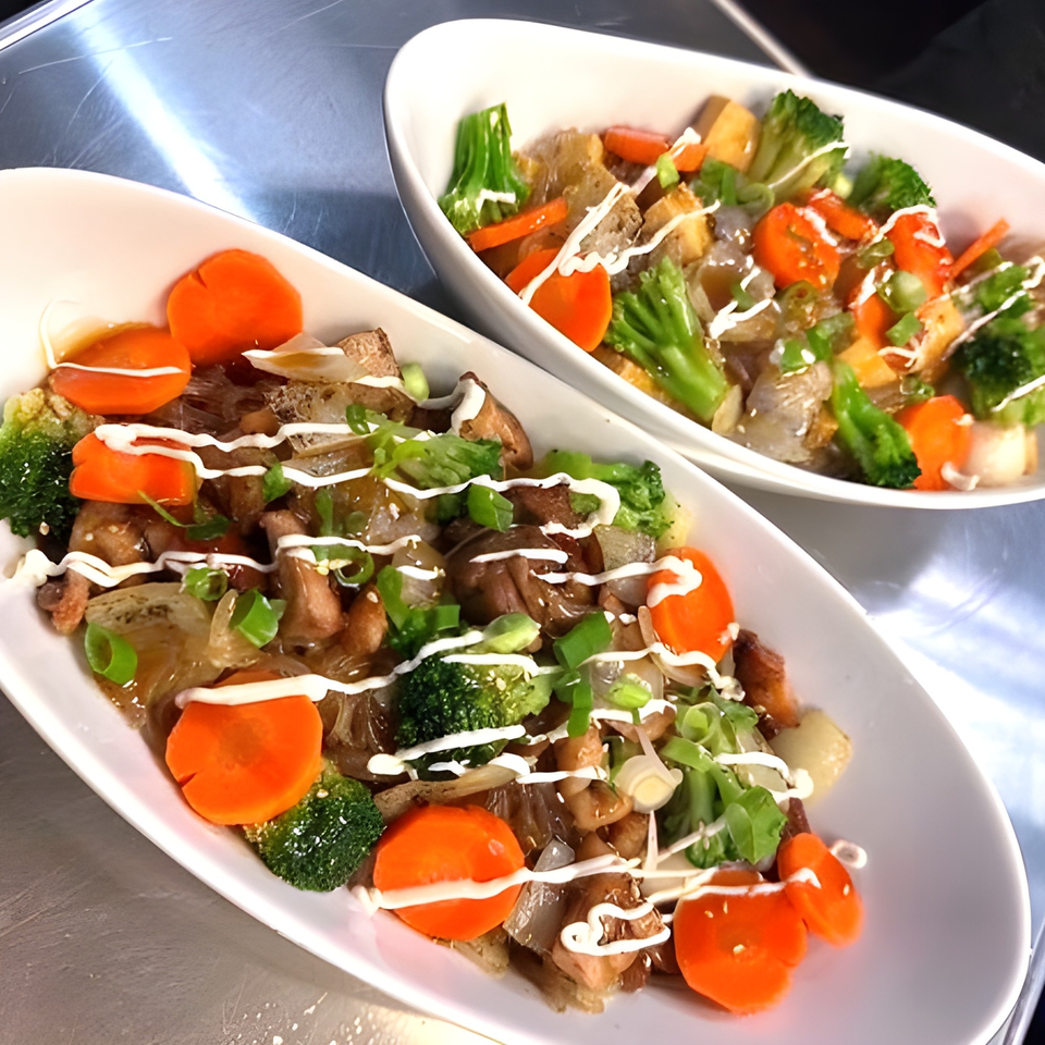 Two white bowls of MoDak Korean chicken, glass noodles, broccoli, carrots, and green onions.