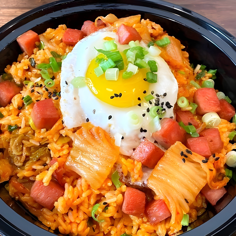 Kimchi fried rice with spam, a fried egg, green onions, and black sesame seeds in a black bowl.