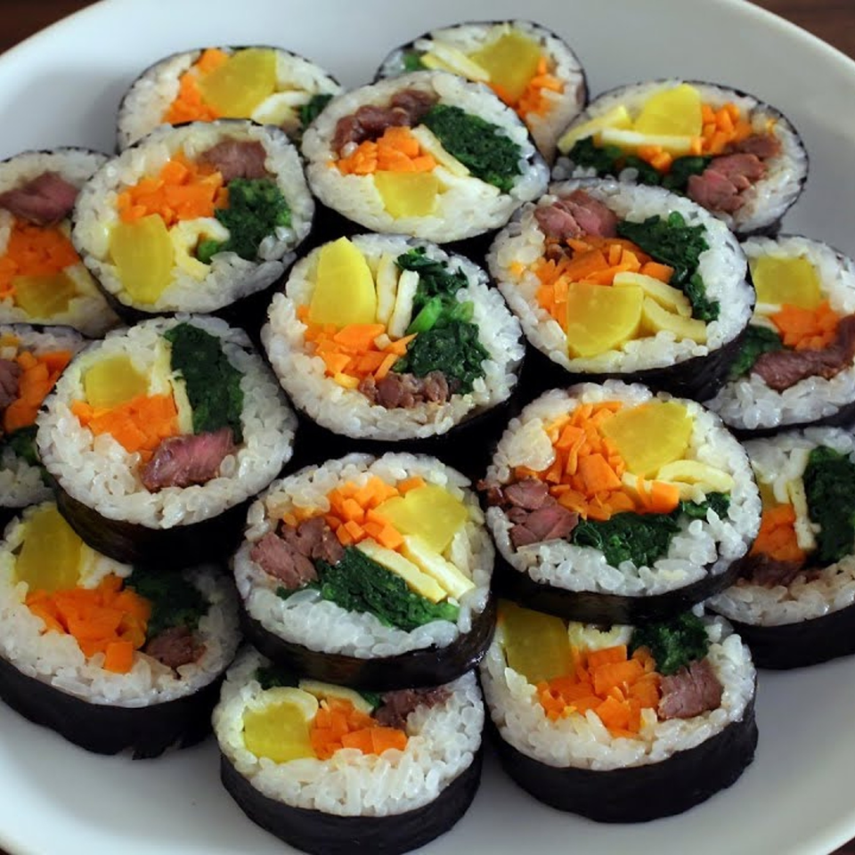 A close-up of several Korean kimbap rolls with beef, spinach, carrots, and yellow pickled radish.